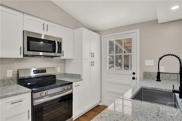 kitchen with stainless steel appliances, a sink, wood finished floors, white cabinetry, and light stone countertops