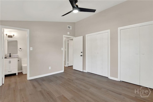 unfurnished bedroom featuring two closets, vaulted ceiling, wood finished floors, ensuite bathroom, and baseboards