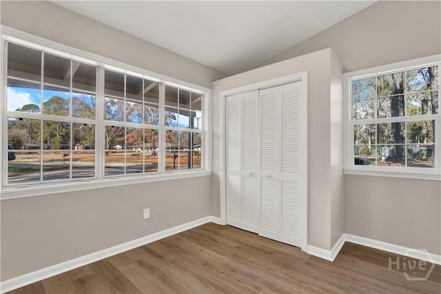 unfurnished bedroom with wood finished floors, baseboards, multiple windows, and lofted ceiling