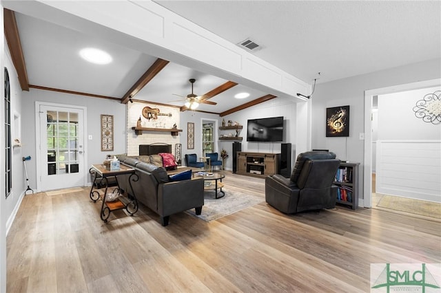 living area with a brick fireplace, light wood-style flooring, beamed ceiling, ceiling fan, and crown molding