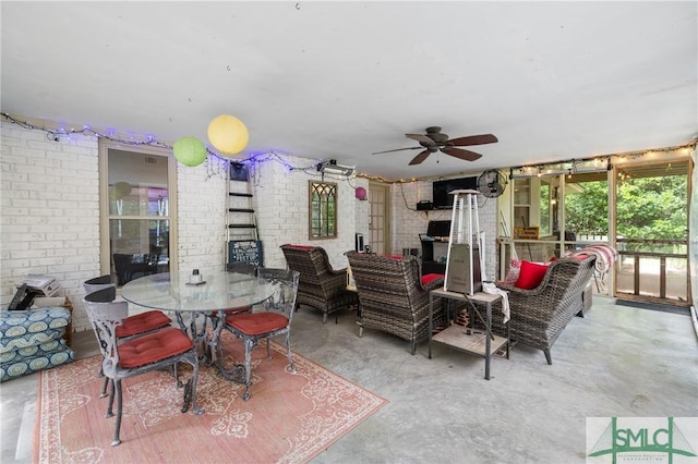 living room with concrete flooring, a ceiling fan, and brick wall