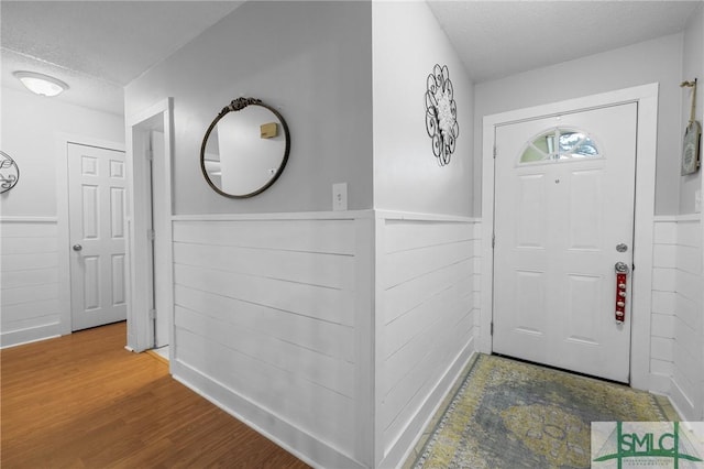foyer entrance with a textured ceiling, a wainscoted wall, and wood finished floors