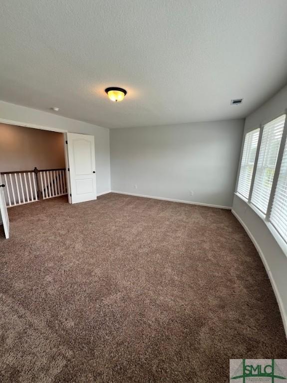 spare room featuring dark colored carpet, baseboards, and a textured ceiling