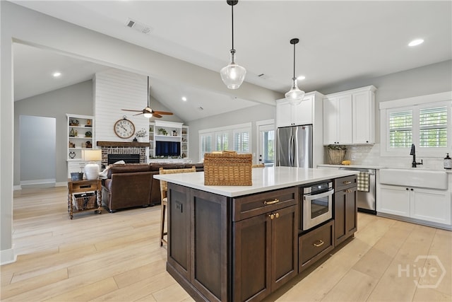 kitchen with appliances with stainless steel finishes, a sink, a fireplace, a ceiling fan, and white cabinetry