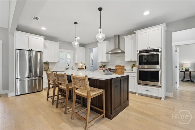kitchen featuring stainless steel appliances, wall chimney range hood, decorative backsplash, a center island, and light countertops