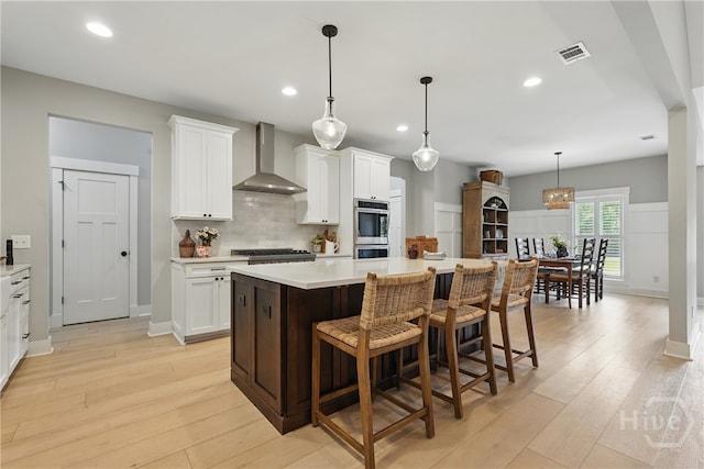 kitchen featuring wall chimney exhaust hood, light wood-style flooring, stainless steel appliances, light countertops, and recessed lighting