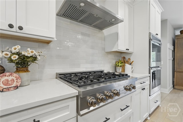 kitchen with wall chimney range hood, appliances with stainless steel finishes, backsplash, white cabinets, and light countertops