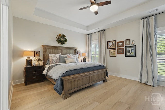 bedroom featuring light wood-style floors, baseboards, and a raised ceiling