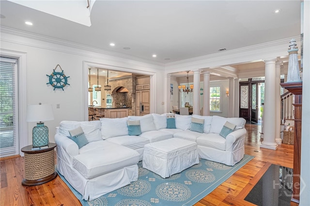 living area with decorative columns, crown molding, light wood-style floors, recessed lighting, and a chandelier