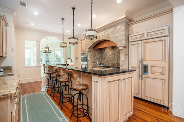 kitchen featuring arched walkways, ornate columns, cream cabinets, a breakfast bar, and crown molding