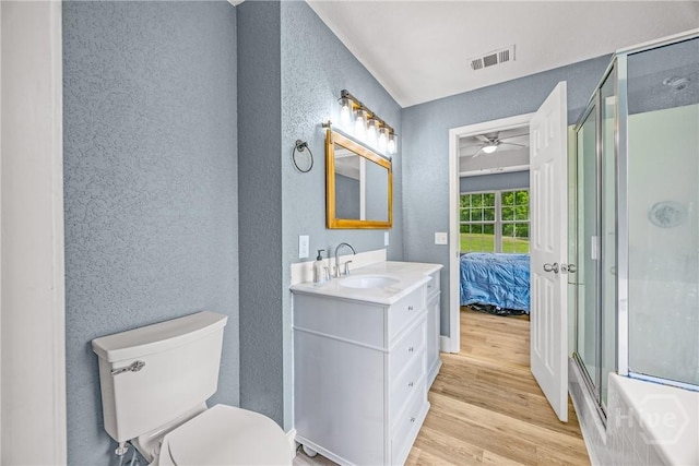 ensuite bathroom featuring a textured wall, wood finished floors, ceiling fan, a shower stall, and toilet