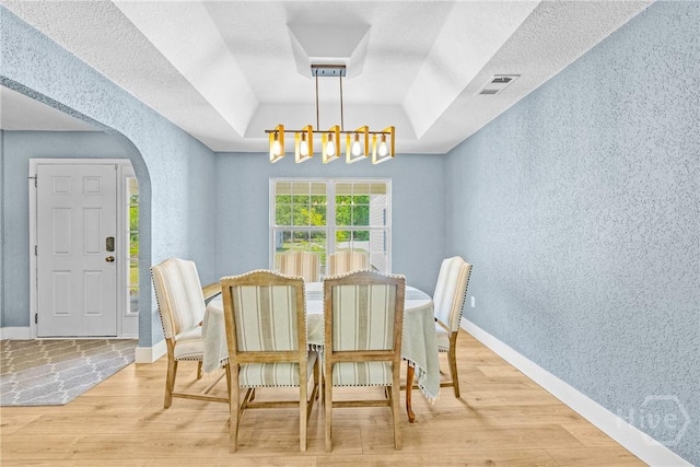 dining space featuring arched walkways, a tray ceiling, wood finished floors, a textured wall, and a chandelier