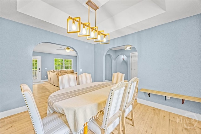 dining room featuring arched walkways, wood finished floors, baseboards, and a textured wall