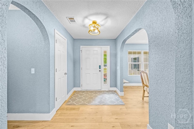 foyer with arched walkways, a textured wall, light wood-style floors, baseboards, and a textured ceiling