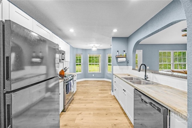 kitchen with appliances with stainless steel finishes, a sink, arched walkways, light wood finished floors, and white cabinetry