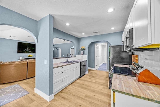 kitchen featuring a sink, arched walkways, black dishwasher, light wood finished floors, and white cabinetry