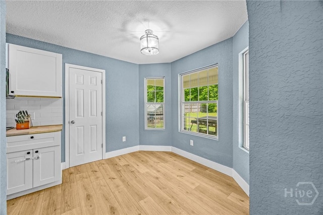 unfurnished dining area with a textured wall, light wood finished floors, a textured ceiling, and baseboards