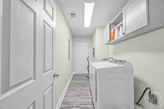 laundry room featuring cabinet space, baseboards, washing machine and dryer, light wood-style flooring, and a textured wall