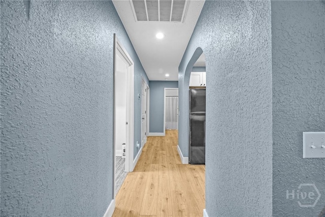 hall with a textured wall, arched walkways, light wood-type flooring, recessed lighting, and baseboards