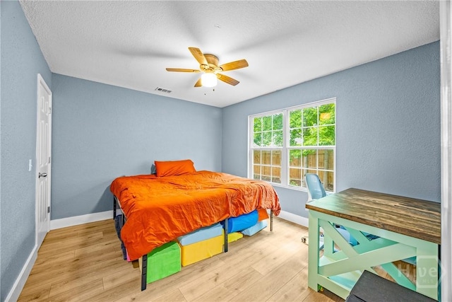 bedroom with wood finished floors, baseboards, a textured wall, ceiling fan, and a textured ceiling