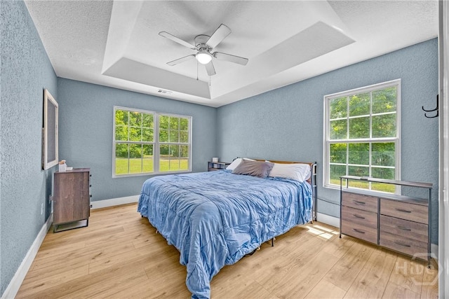 bedroom with a textured wall, a raised ceiling, wood finished floors, multiple windows, and a textured ceiling