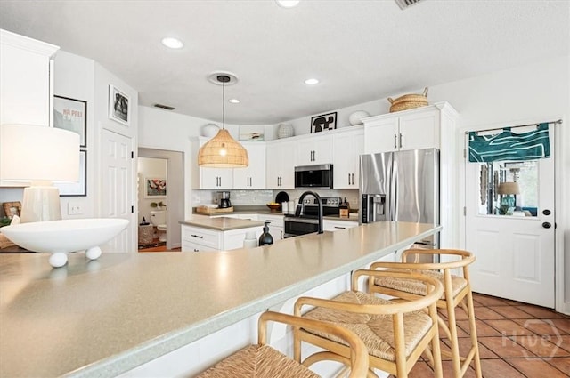 kitchen featuring appliances with stainless steel finishes, white cabinets, a breakfast bar area, light countertops, and recessed lighting