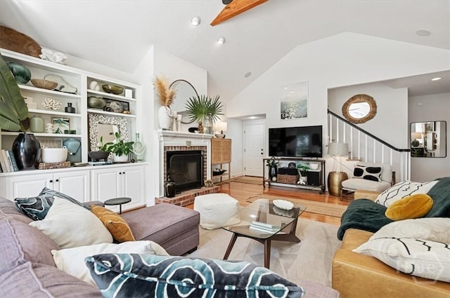 living room with light wood-style floors, vaulted ceiling, stairs, and a brick fireplace