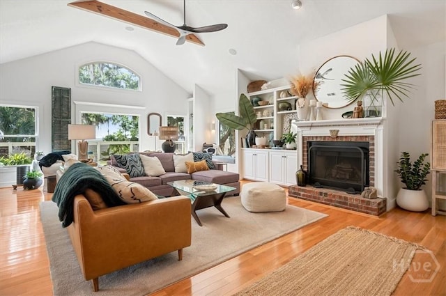 living room featuring ceiling fan, a fireplace, wood finished floors, and high vaulted ceiling