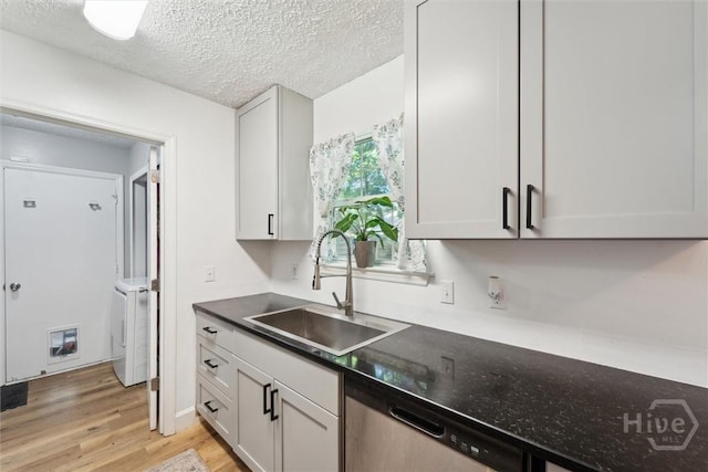 kitchen featuring a sink, dishwasher, washer / clothes dryer, light wood-type flooring, and dark countertops