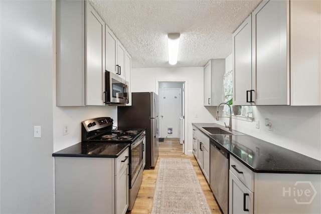 kitchen featuring stainless steel appliances, a sink, light wood-type flooring, a textured ceiling, and dark countertops