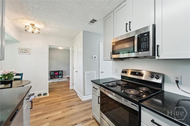 kitchen with appliances with stainless steel finishes, light wood-style flooring, a textured ceiling, dark stone countertops, and white cabinets