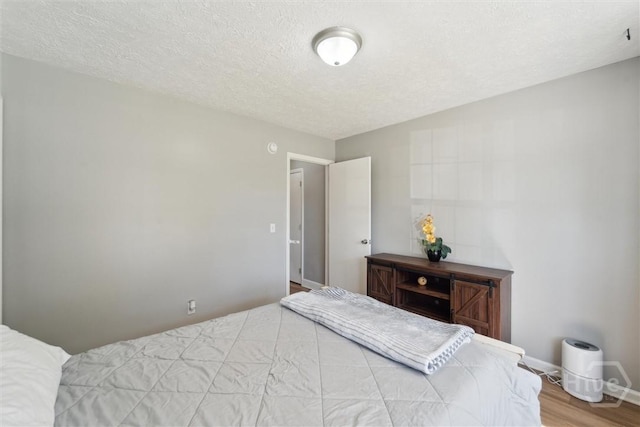 bedroom with wood finished floors, a textured ceiling, and baseboards
