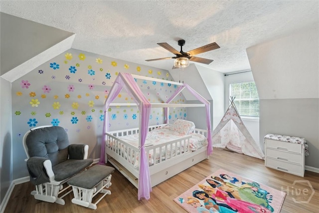 bedroom with a textured ceiling, wallpapered walls, wood finished floors, lofted ceiling, and ceiling fan