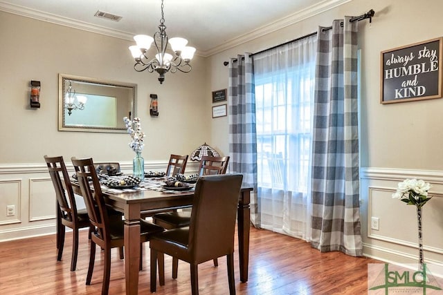 dining space featuring a chandelier, wood finished floors, crown molding, wainscoting, and a decorative wall