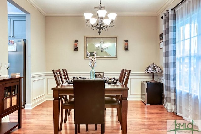 dining area featuring a chandelier, light wood-style flooring, crown molding, wainscoting, and a decorative wall