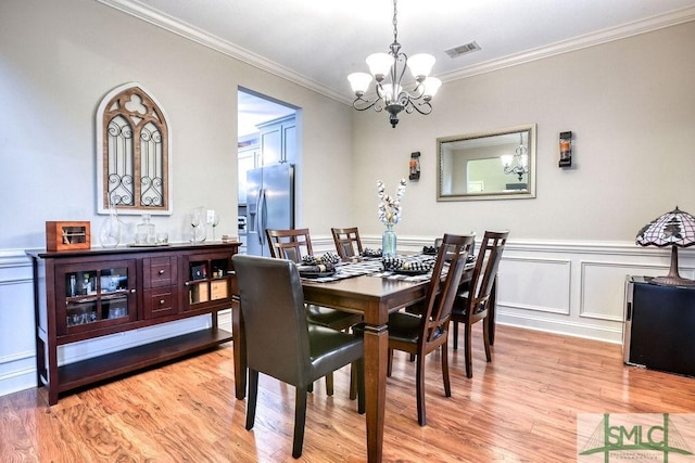 dining area with a chandelier, crown molding, light wood-type flooring, wainscoting, and a decorative wall
