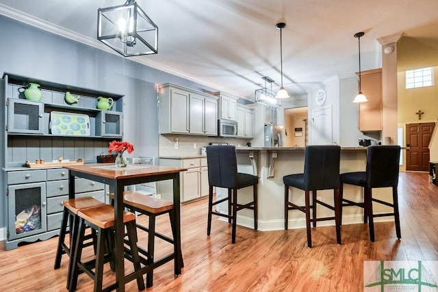 kitchen featuring stainless steel appliances, ornamental molding, light wood-style floors, a kitchen bar, and pendant lighting