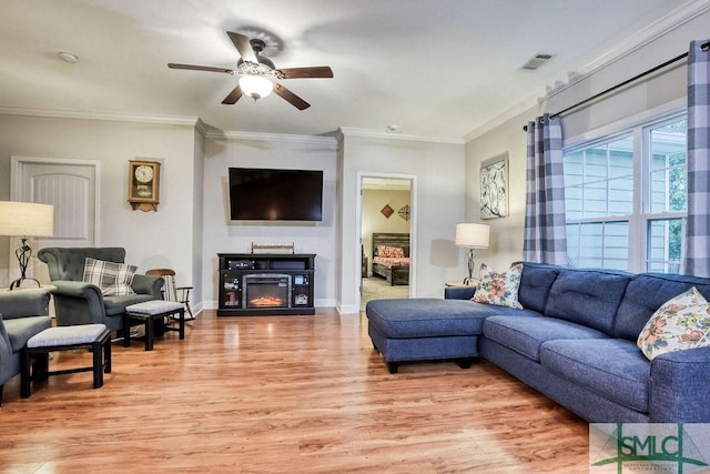 living area featuring light wood-type flooring, a ceiling fan, ornamental molding, a glass covered fireplace, and baseboards