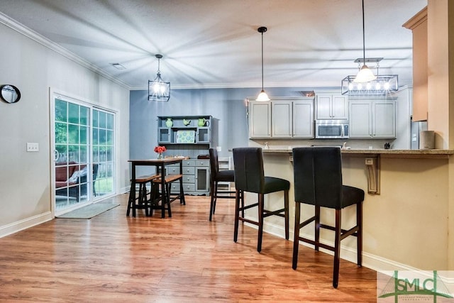 kitchen featuring stainless steel microwave, light wood-style flooring, a breakfast bar area, decorative light fixtures, and baseboards