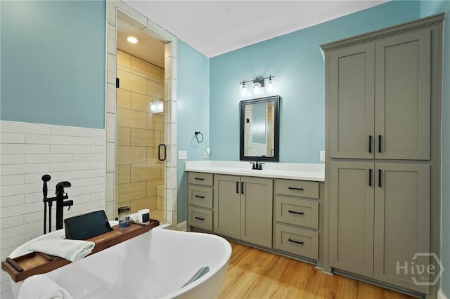 bathroom with tile walls, a stall shower, vanity, a soaking tub, and wood finished floors