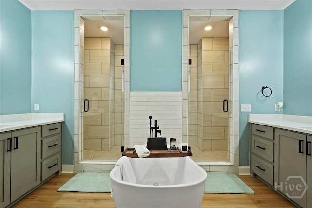 full bath featuring vanity, a stall shower, wood finished floors, a freestanding tub, and baseboards