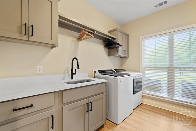 clothes washing area featuring washing machine and clothes dryer, cabinet space, and light wood-style flooring