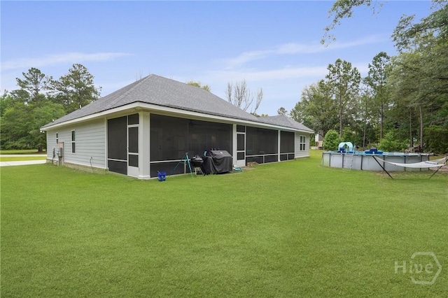 rear view of property featuring a sunroom, a lawn, a covered pool, and roof with shingles