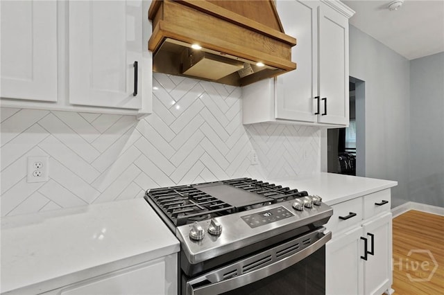 kitchen with stainless steel range with gas stovetop, custom range hood, light countertops, white cabinets, and decorative backsplash