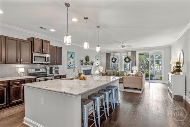 kitchen with stainless steel appliances, a sink, ornamental molding, a center island with sink, and a ceiling fan