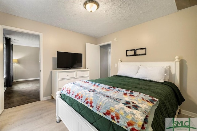 bedroom with light wood finished floors, baseboards, and a textured ceiling