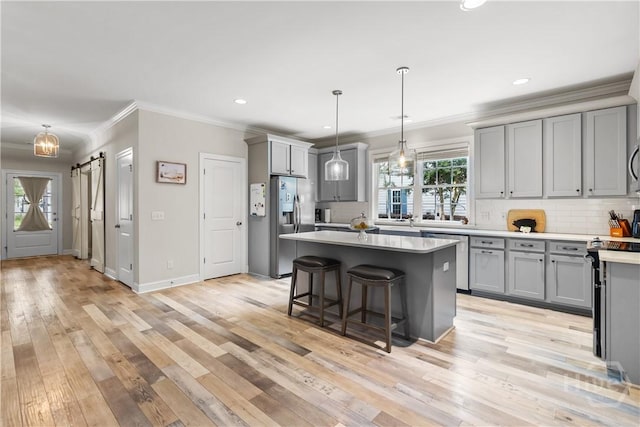 kitchen with gray cabinetry, stainless steel appliances, a barn door, ornamental molding, and backsplash