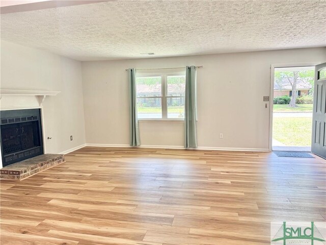 932 Millstream Ct, Savannah, GA 31419 - unfurnished living room featuring plenty of natural light, light wood finished floors, a fireplace, a textured ceiling, and baseboards