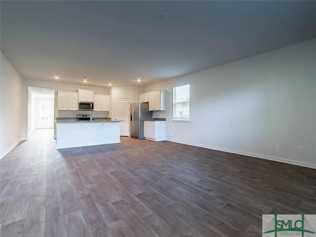 kitchen with appliances with stainless steel finishes, open floor plan, dark wood finished floors, and baseboards