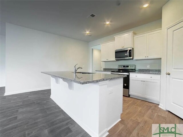 kitchen with stainless steel appliances, a sink, a center island with sink, dark wood-type flooring, and stone countertops